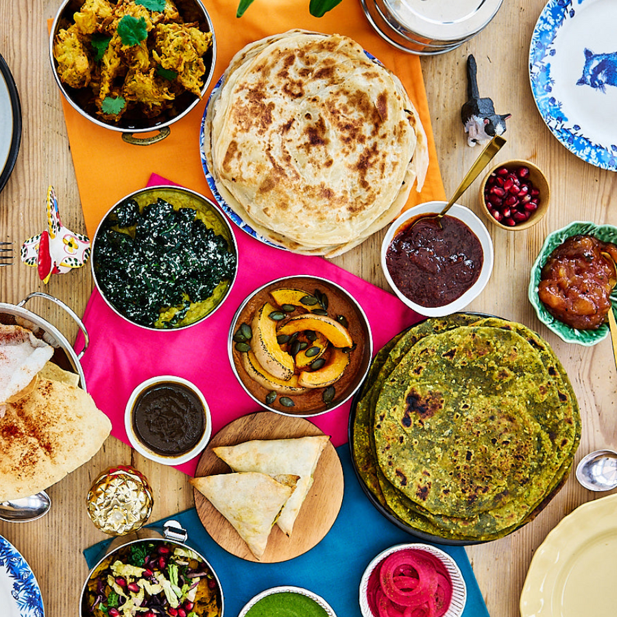 Diverse array of food items on a wooden table with colorful plates and flowers.